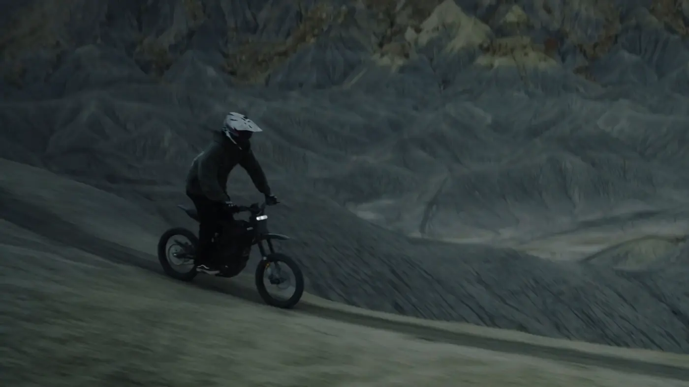 Rider pe cross electric pe o pantă de rocă gri, cu munți în fundal